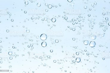 An underwater photograph of bubbles on a clear blue background.  The bubbles are randomly dispersed.  The bubbles vary in size with most being very small and a few being larger.  The background is a translucent blue.  The light comes from the bottom of the photo, making the bottom of the background very light blue, while the top is a darker shade.  The water is free of any visible impurities.  The bubbles seem to be largely concentrated in the upper right portion of the center of the photo, as well as the upper middle.